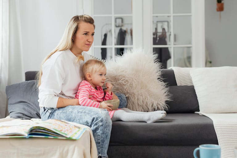 A woman and her toddler daughter relaxing on a couch in a cozy living room setting.