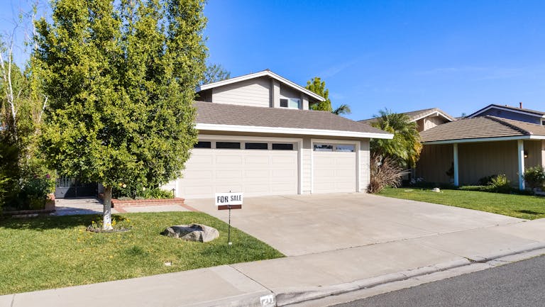 Beautiful suburban house with a for sale sign on a sunny day.