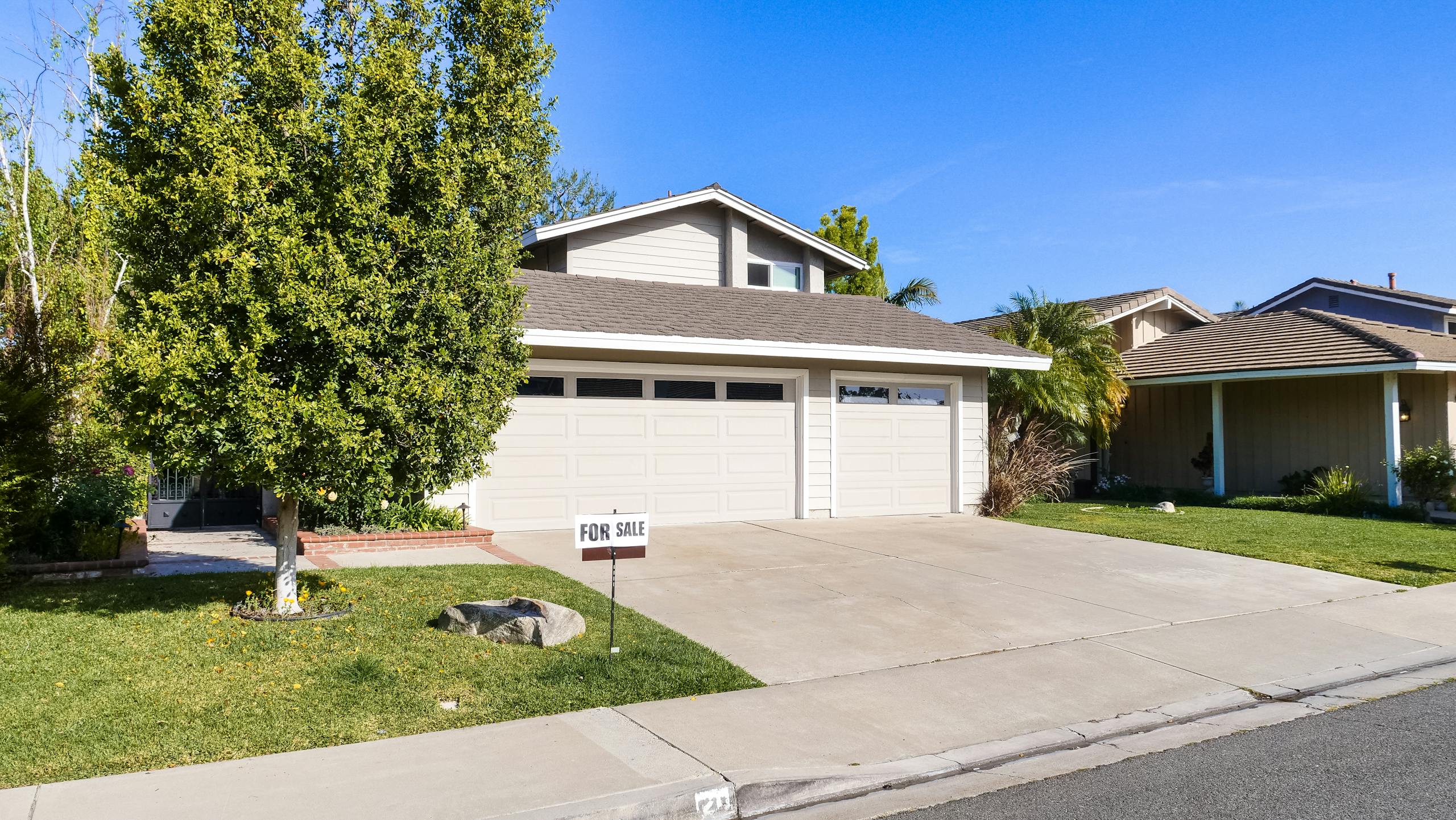 Beautiful suburban house with a for sale sign on a sunny day.