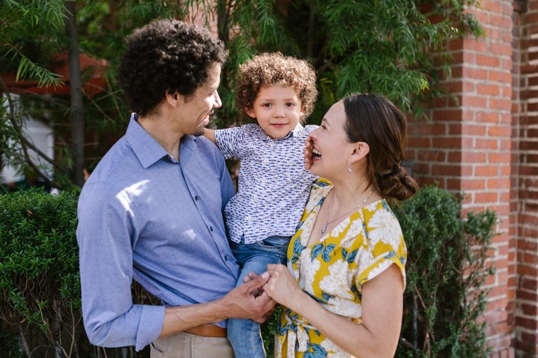 Smiling parents embracing their son outside, enjoying a sunny spring day.